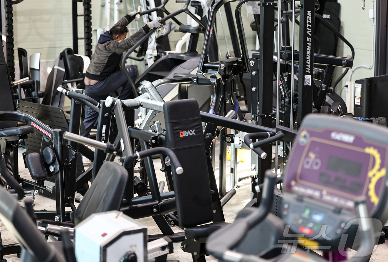 Used gym machines crowd a fitness equipment resale store in Yongin, Gyeonggi Province, on Feb. 3, as a worker arranges the inventory. (Newsis)