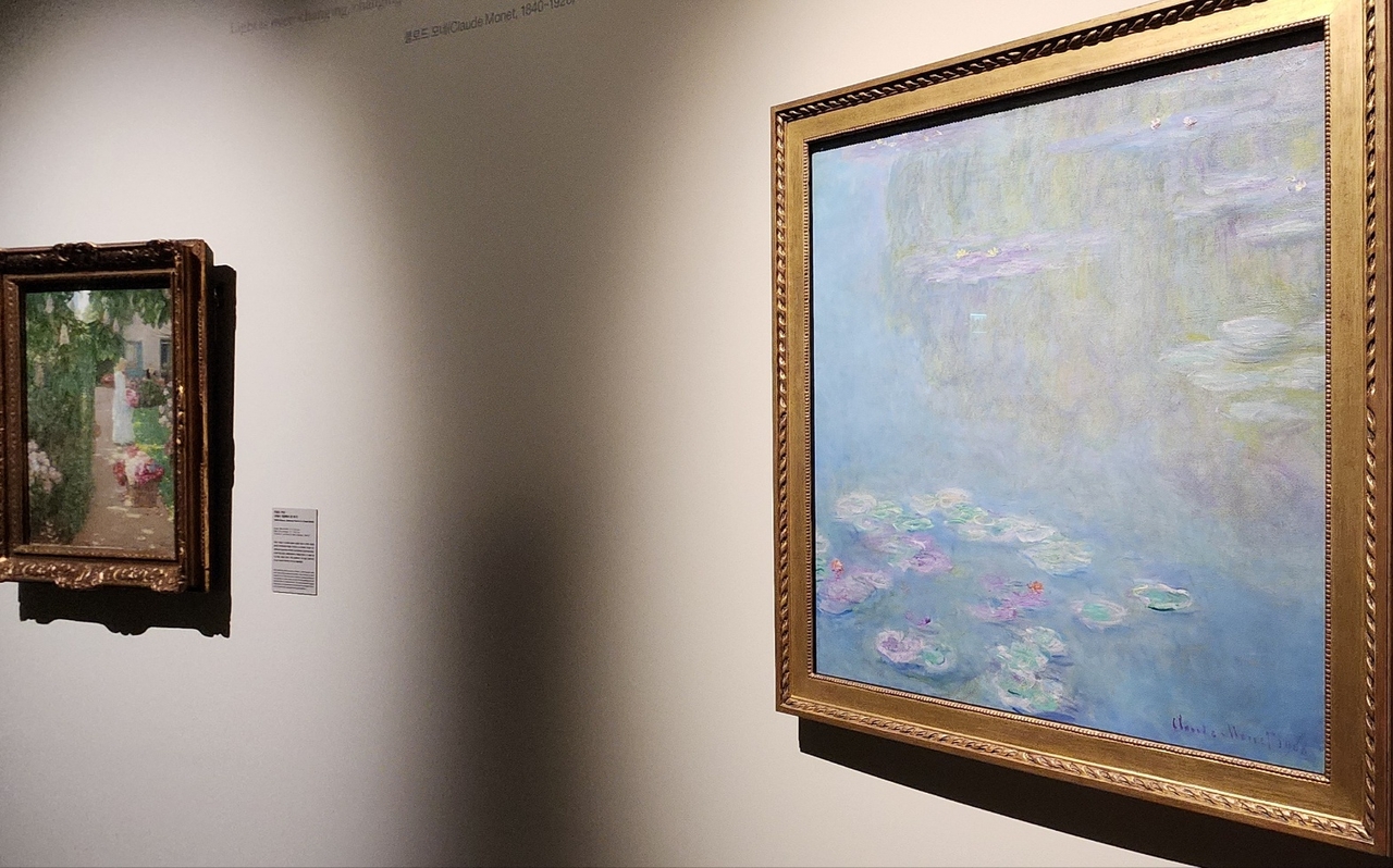 “Water Lilies” by Claude Monet (right) and “Gathering Flowers in a French Garden” by Childe Hassam at The Hyundai Seoul in Yeouido, Seoul (Choi Si-young/The Korea Herald)