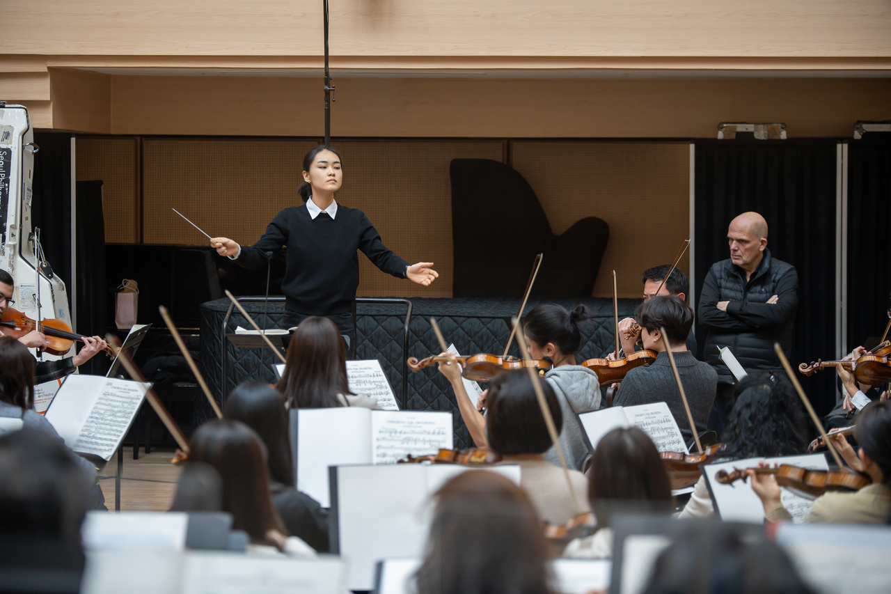 Seoul Philharmonic Orchestra's Artistic Director Jaap van Zweden (right) watches as Shin Ju-ya, a participant of the SPO Conducting Fellowship, leads the SPO during a rehearsal on Feb. 26 at the Sejong Center for the Performing Arts in Seoul. (SPO)