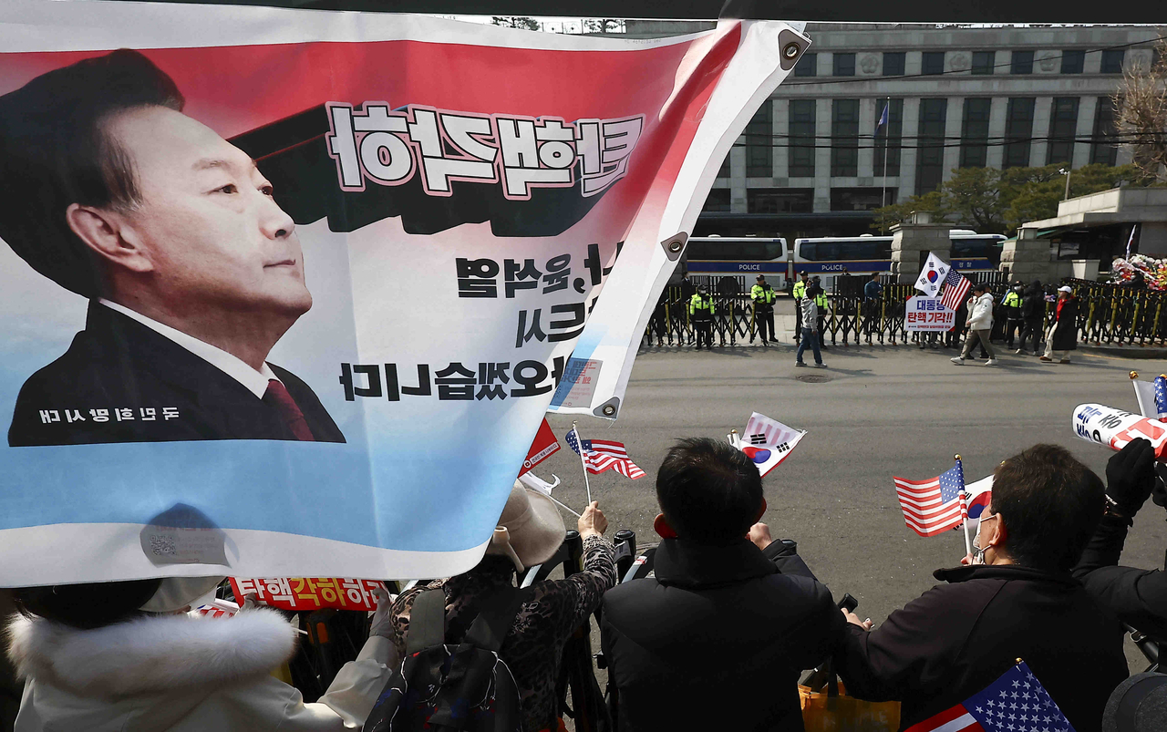 People wave national flags of South Korea and the United States, calling for the Constitutional Court to overturn President Yoon Suk Yeol's impeachment motion, in front of the Constitutional Court in Seoul on Monday. (Newsis)
